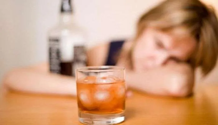Pessoa debruçada sobre a mesa com um copo e garrafa de bebida alcoólica