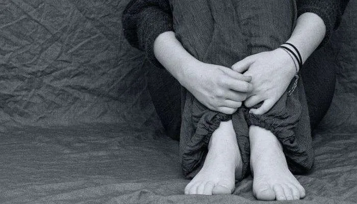 Imagem em preto e branco com uma pessoa sentada no chão com joelhos no peito e braços em volta